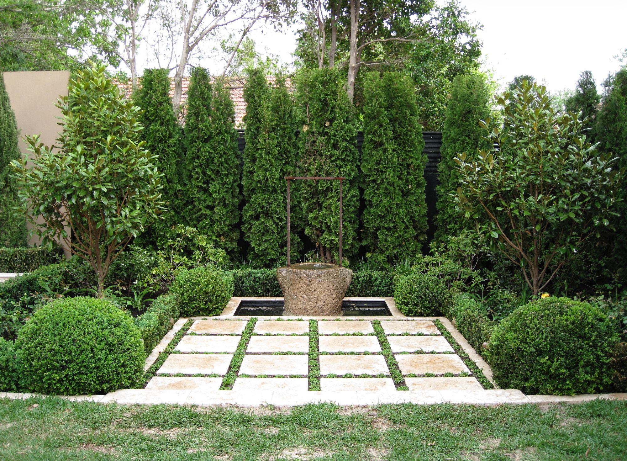 Brighton garden — a formal courtyard with stone water feature, pencil pines and chequerboard paving